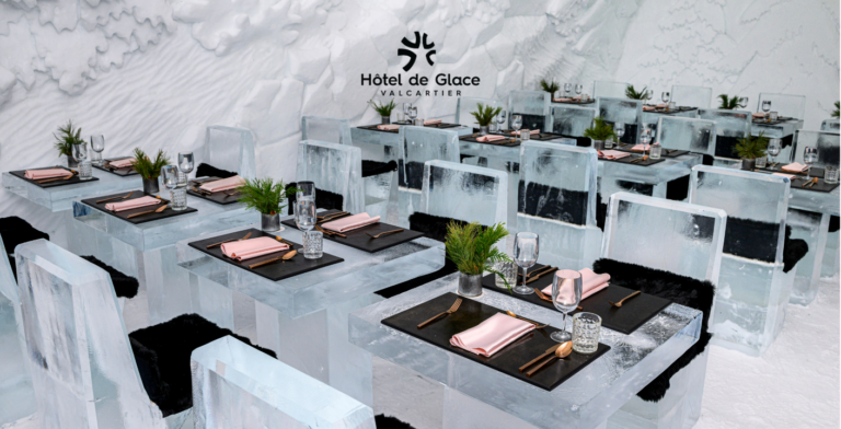 La salle à manger du restaurant de glace donne l’impression d’entrer dans une véritable cathédrale nordique, entièrement façonnée dans la neige et la glace. Les murs, délicatement sculptés de motifs forestiers et de paysages hivernaux, enveloppent l’espace d’une blancheur apaisante, réchauffée par un éclairage doux et bien pensé. Les tables et les chaises, taillées dans des blocs de glace cristalline, sont habillées de surfaces mates et de peaux de fourrure