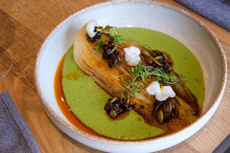 Un chou rôti repose sur une sauce verte lisse et éclatante. un pipián, qui tapisse le fond de l’assiette comme un velours. Autour, un filet d’huile rouge orangé apporte contraste et chaleur visuelle.