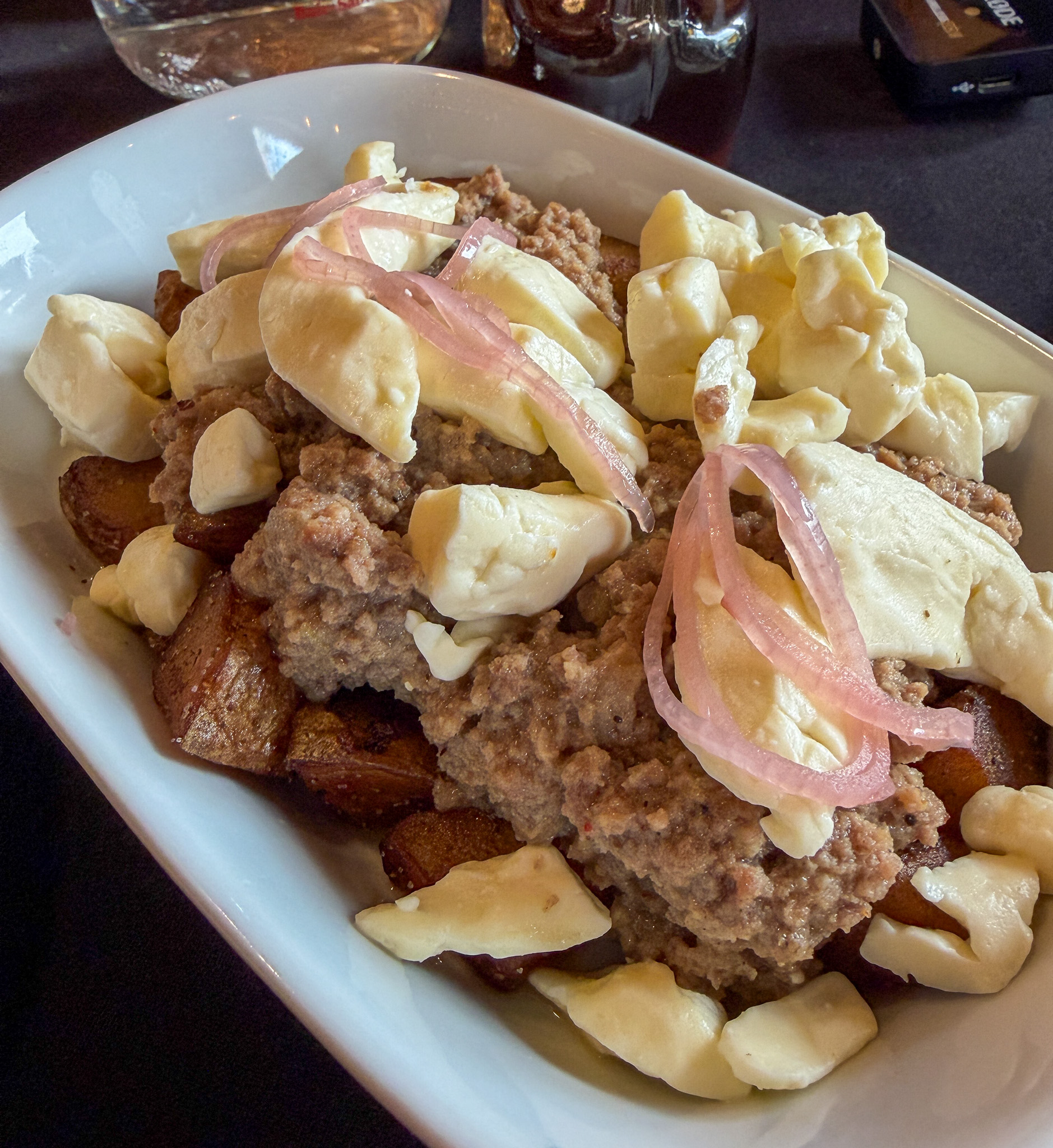 une poutine avec une sauce aux cretons de veau, avec des oignons marinés rouges sur le dessus.